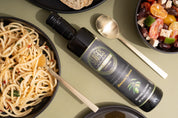 Stavros Kalamata Reserve Extra Virgin Olive Oil bottle photographed in aerial view next to pasta dish and greek salad bowl