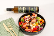 Stavros Kalamata Reserve Extra Virgin Olive Oil bottle photographed laying down next to a closeup of a Greek Salad